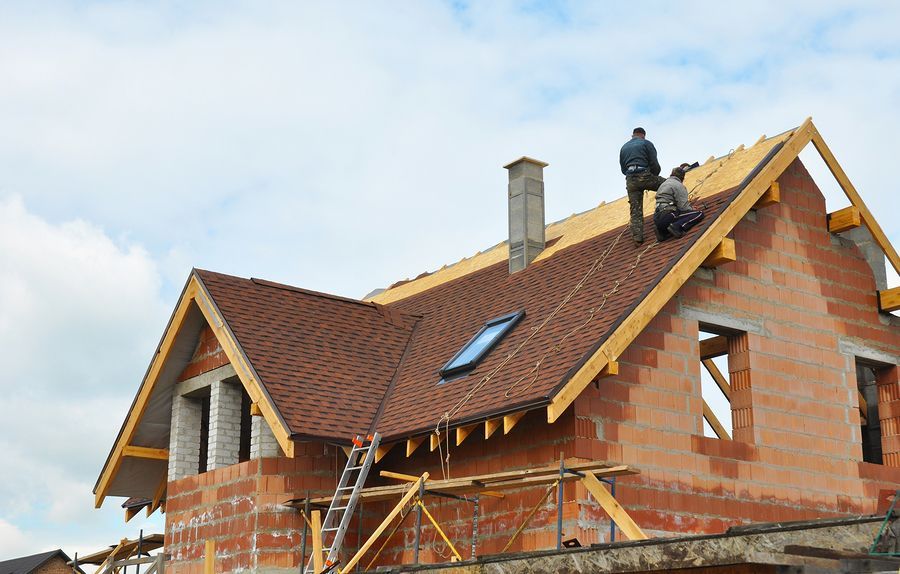 two men are working on the roof of a brick house