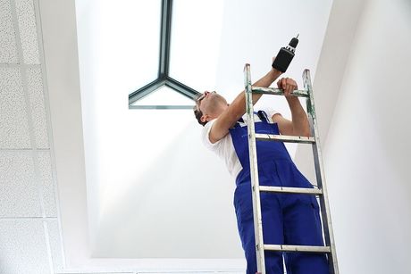 a man is standing on a ladder working on a light fixture .