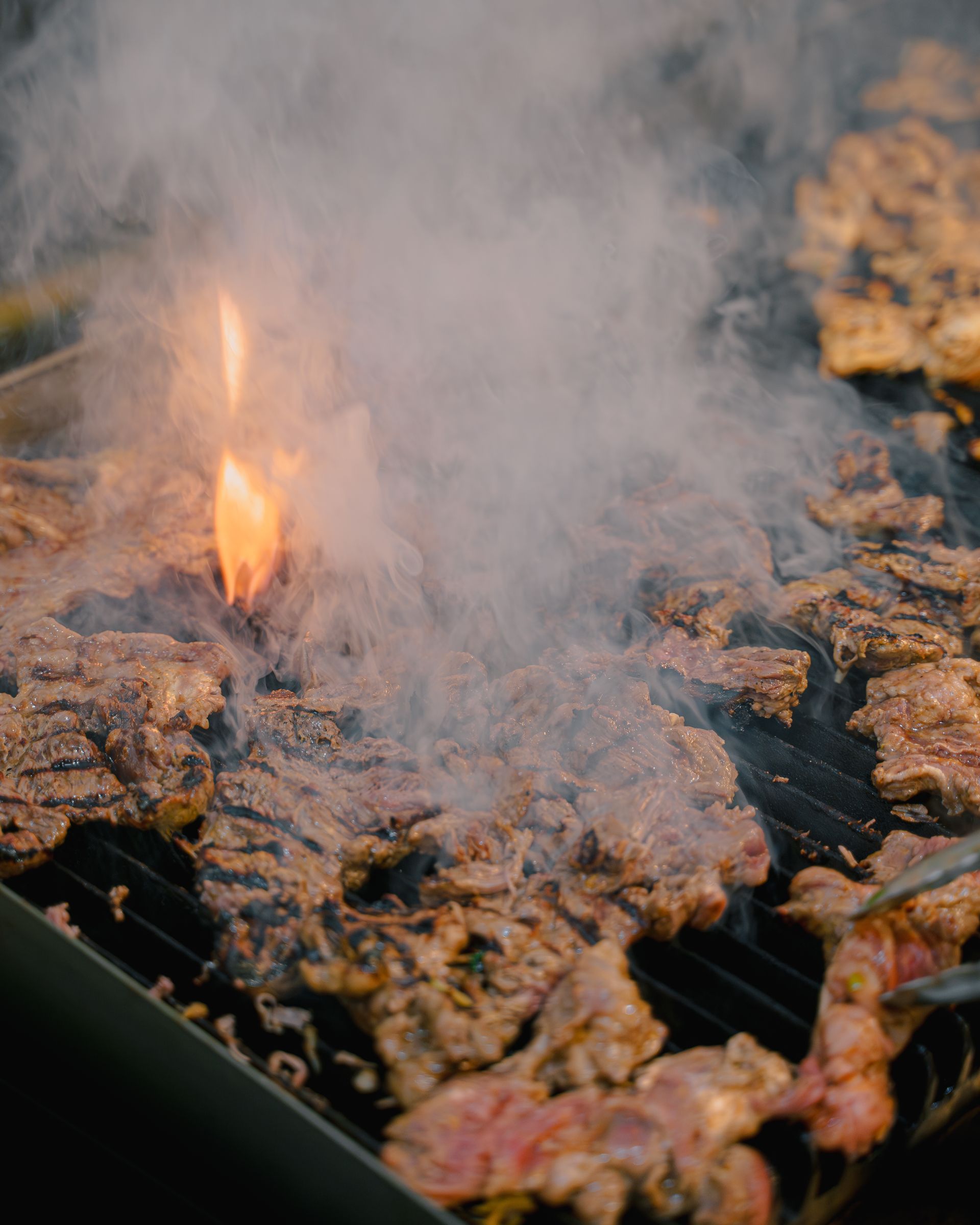A close up of a grill with meat and smoke coming out of it.