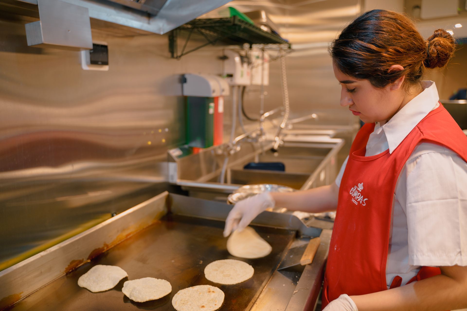 A woman is cooking tortillas on a grill in a kitchen.