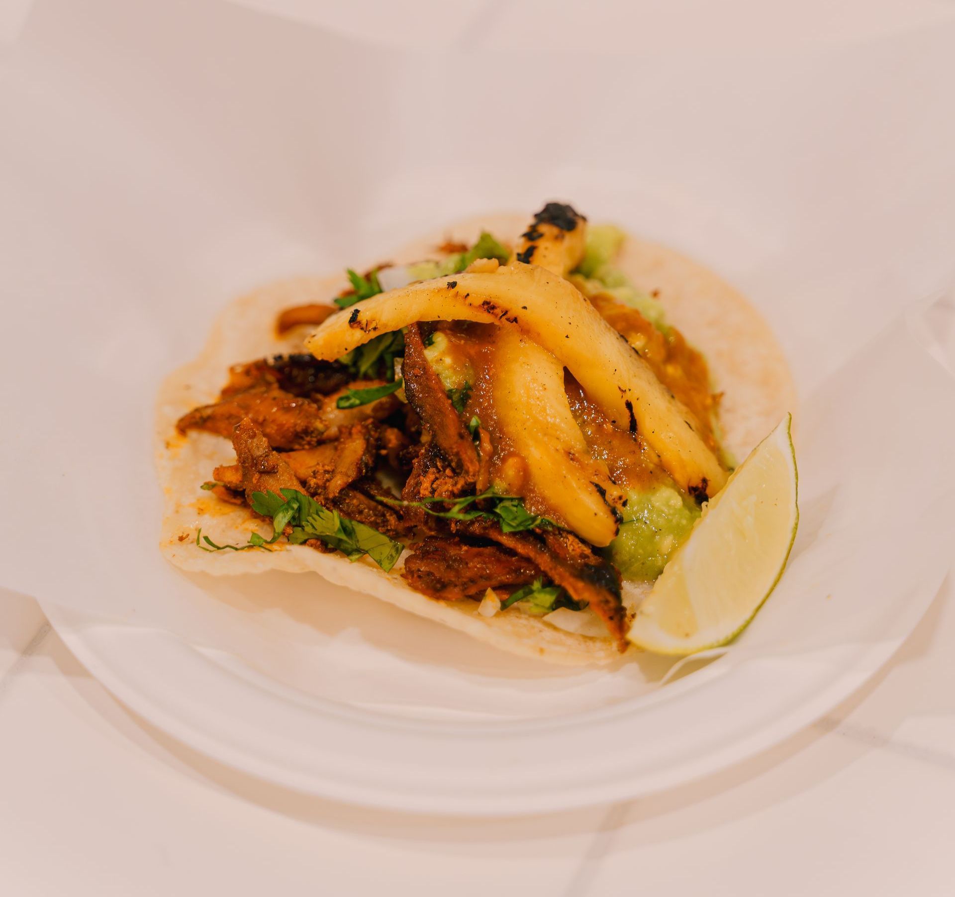 A taco with french fries and a lime wedge on a white plate.