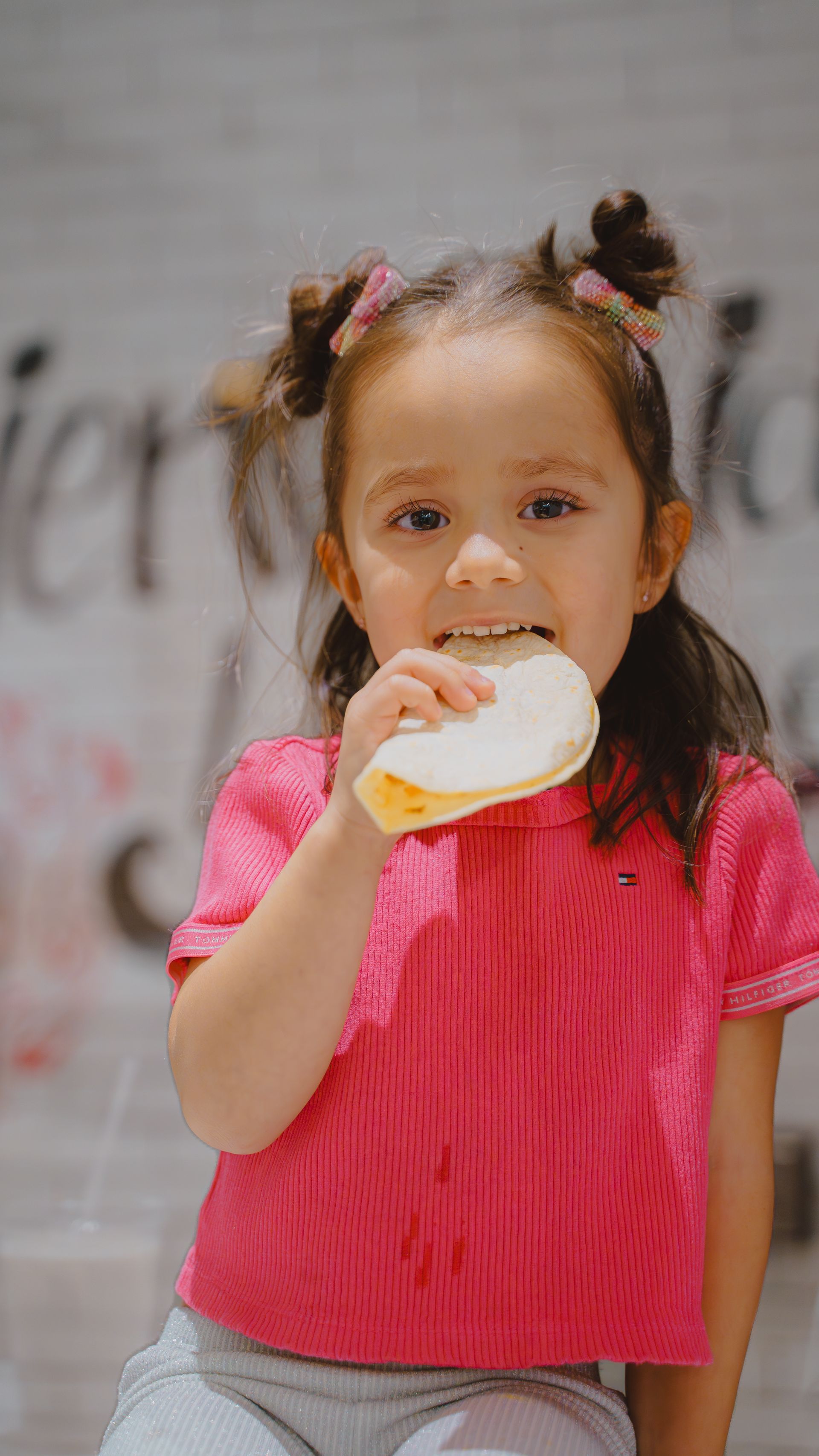 A little girl in a pink shirt is eating a sandwich.