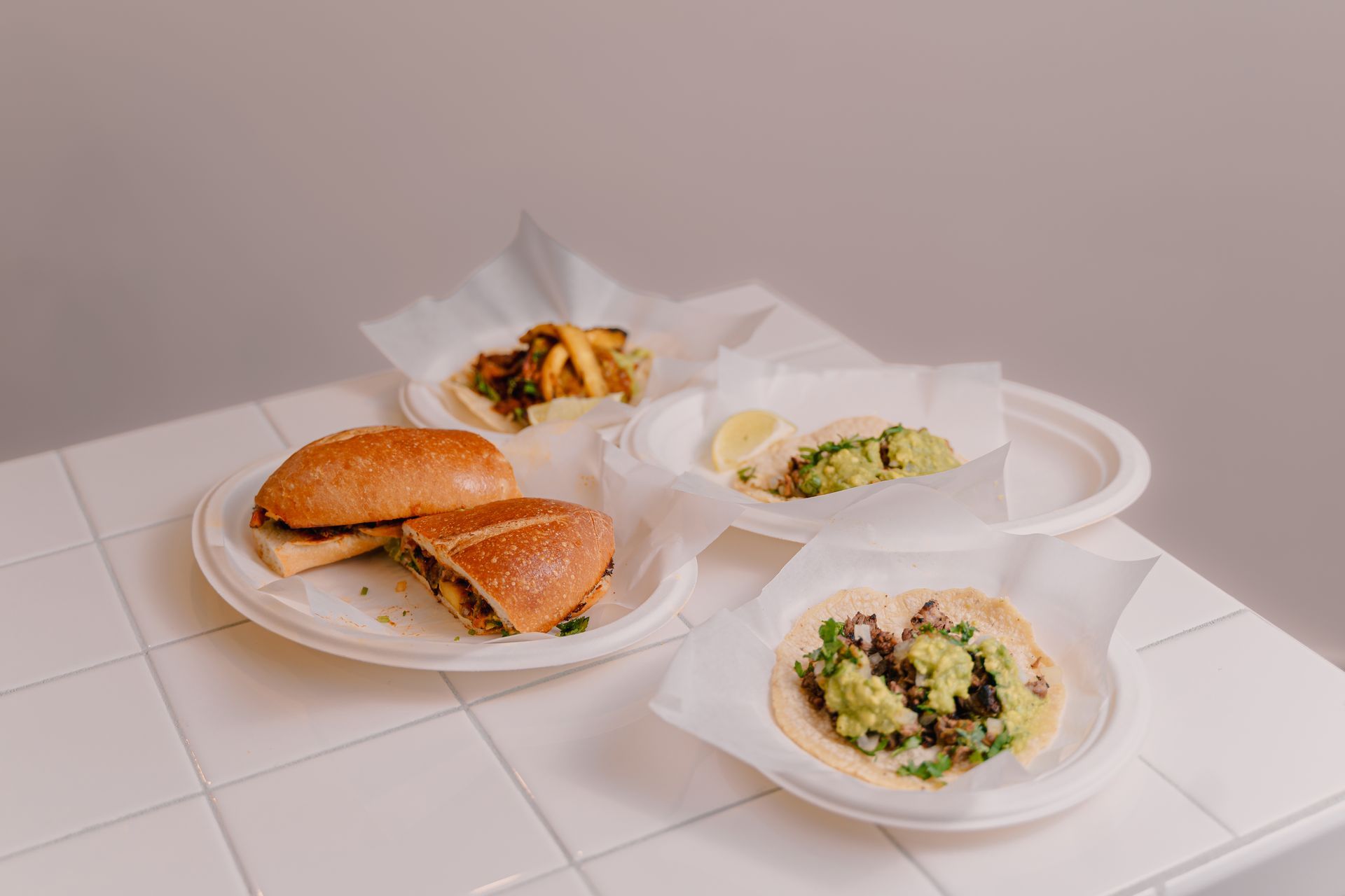 Three plates of food are sitting on a white tiled table.