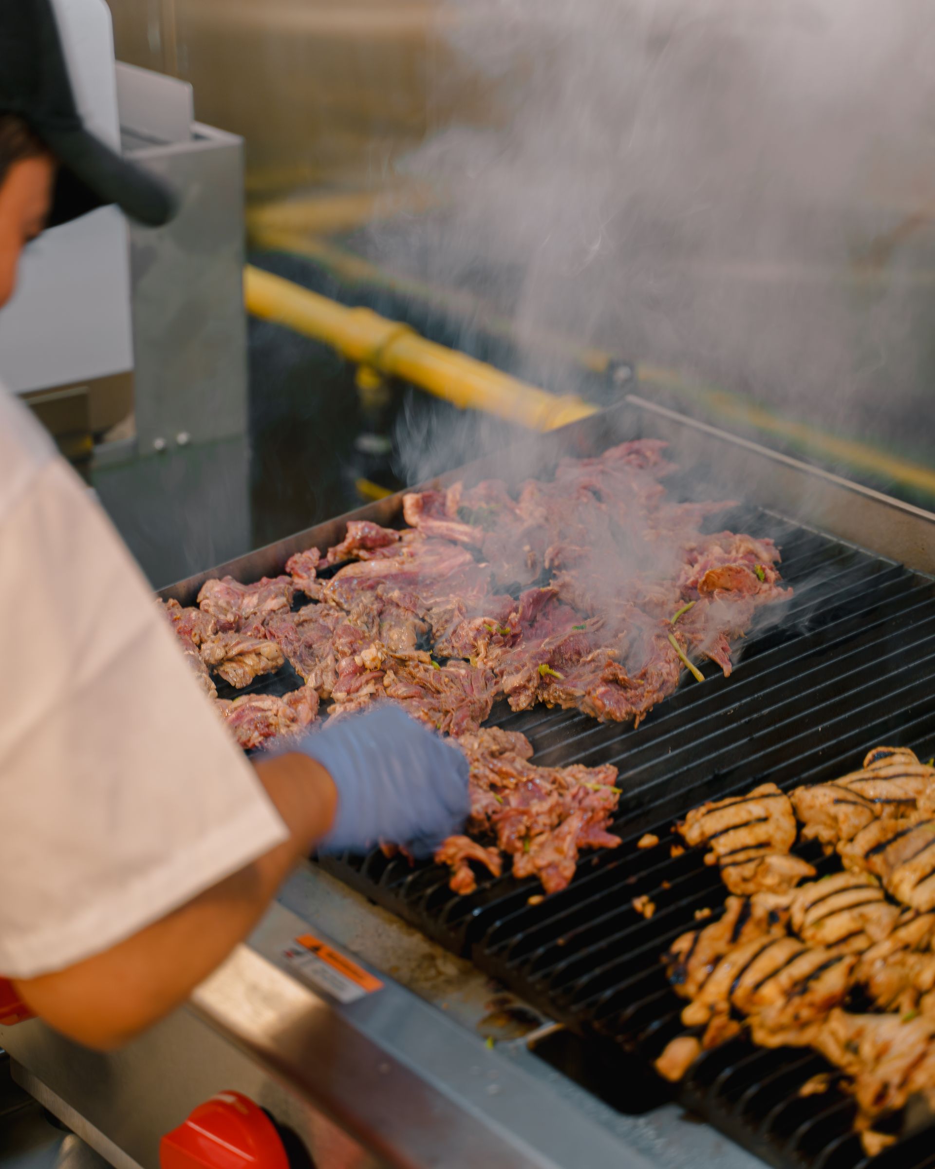 A man is cooking meat on a grill in a kitchen.