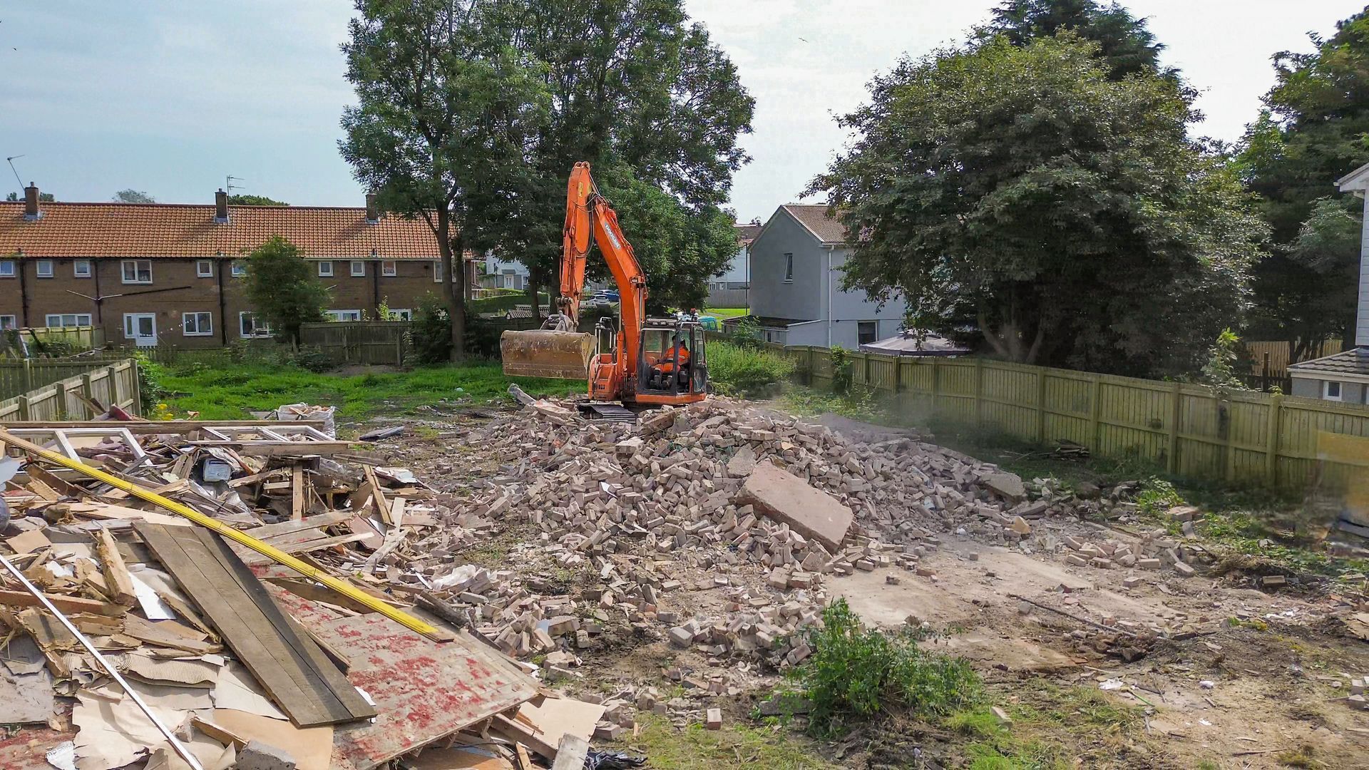Image of the excavator scraping up the remaining rubble from the demolition of the building.
