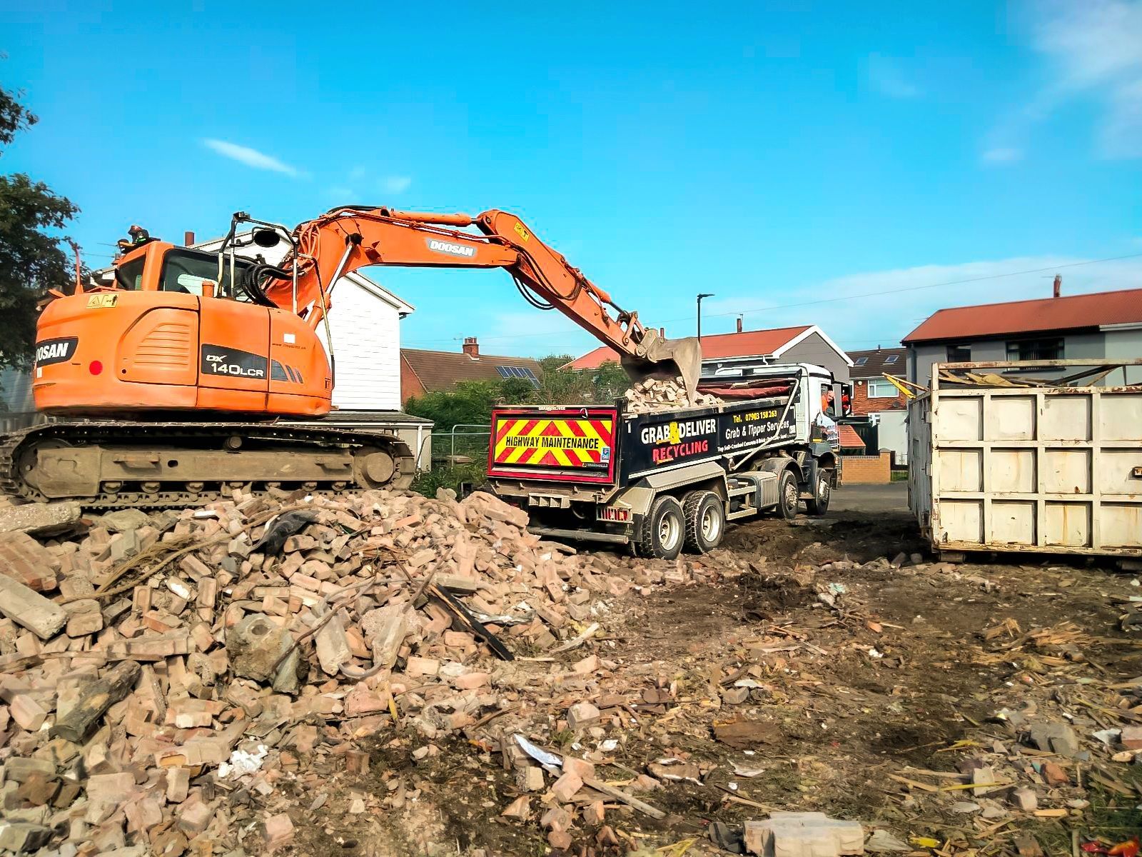 Image of the excavator filling the respective roll-on-off skips with debris and waste from the demolition of the building.