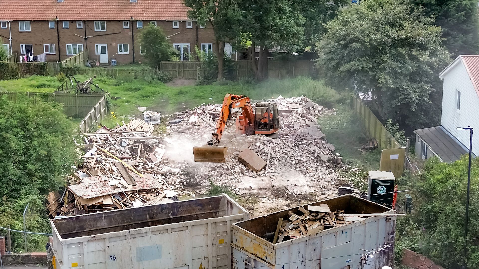 Image of the excavator scraping up the remaining rubble from the demolition of the building.