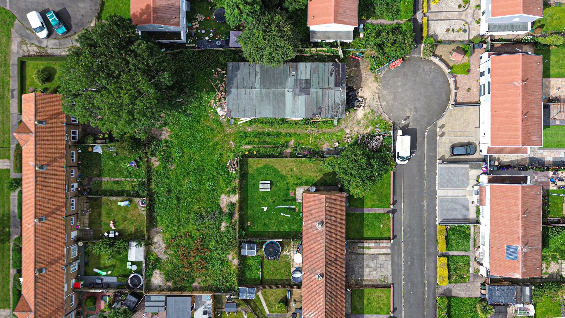 Ariel view of the Long Benton Site.  Large L-shaped plot of land, at the end of a cul-de-sac covered in greenery and trees.  On the land is an old, derelict, concreate prefab building that served over the years as a scout hut.