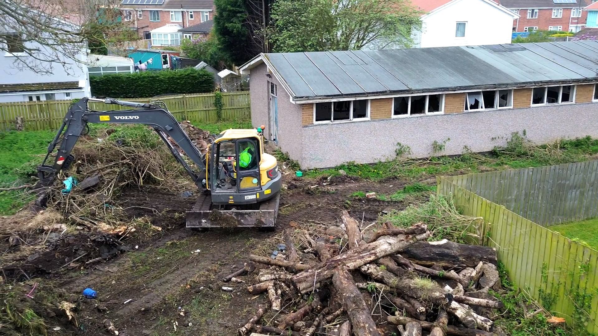 Excavator is moving huge cut down trees into piles.