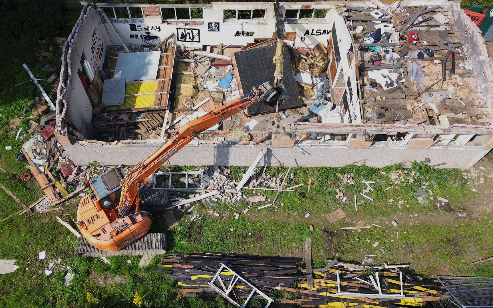 A side view image of the excavator removing the metal girders from the roof of the building.