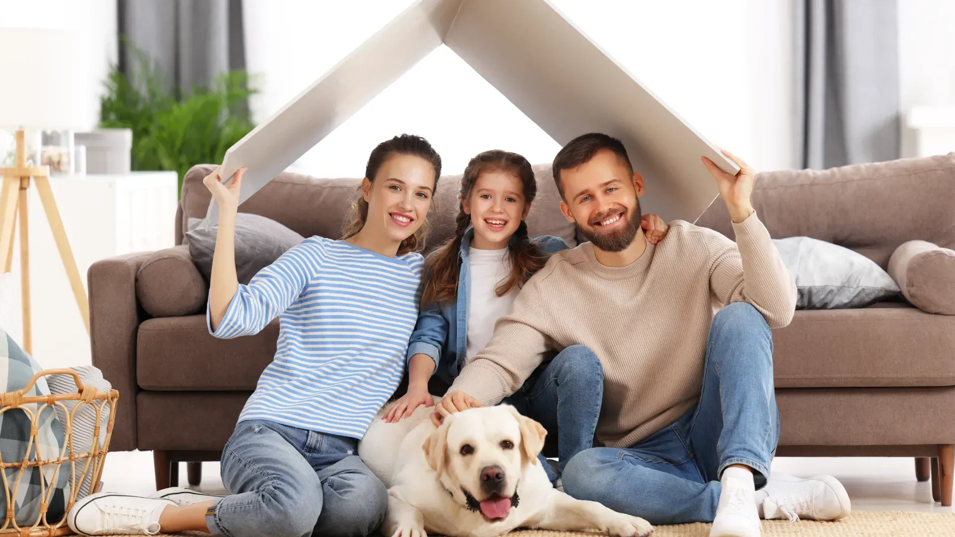 A family is sitting on the floor with a dog under a cardboard house.