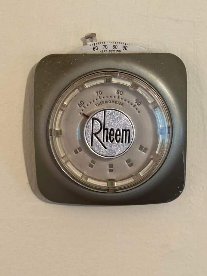 A rheem thermostat is hanging on a white wall.