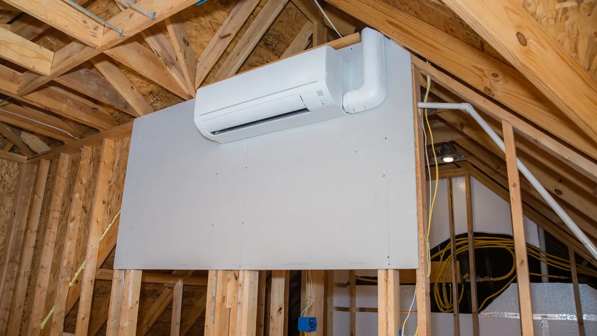 A wall mounted air conditioner is hanging from the ceiling of a house under construction.