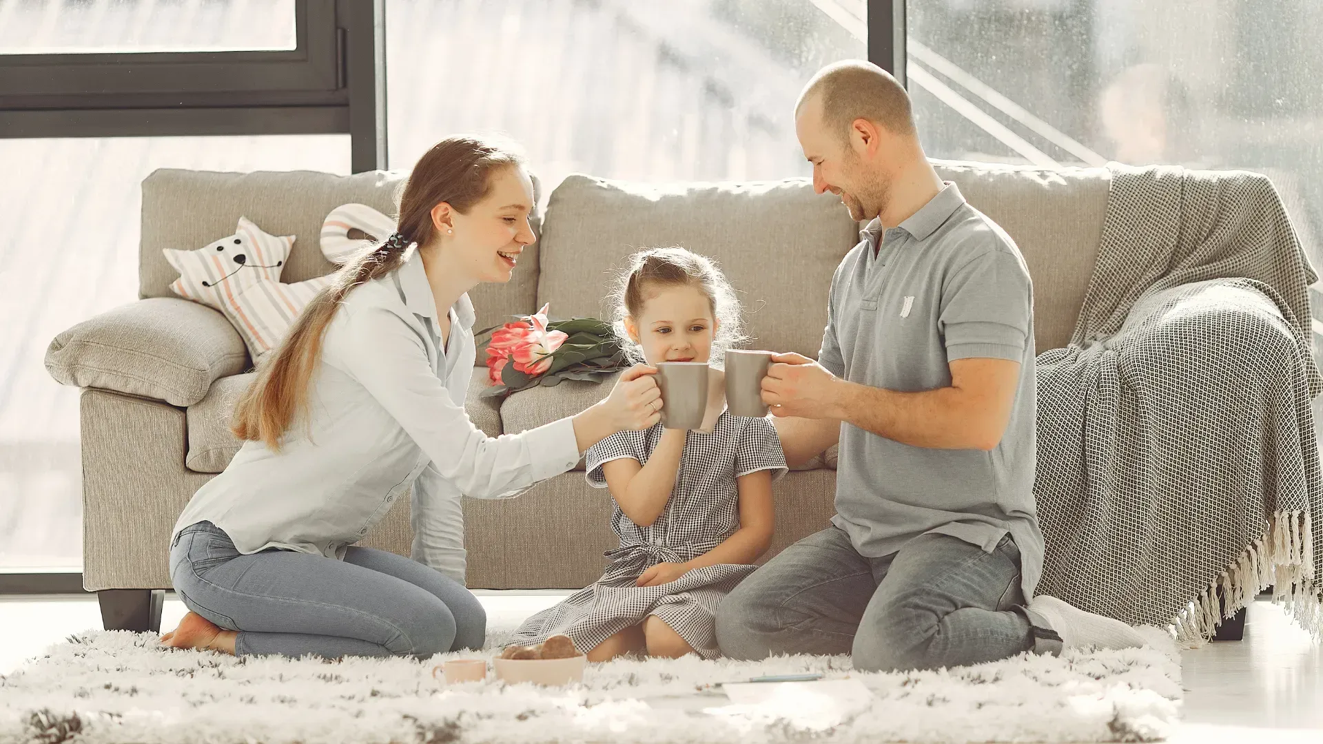 A family is sitting on the floor in front of a couch drinking coffee.