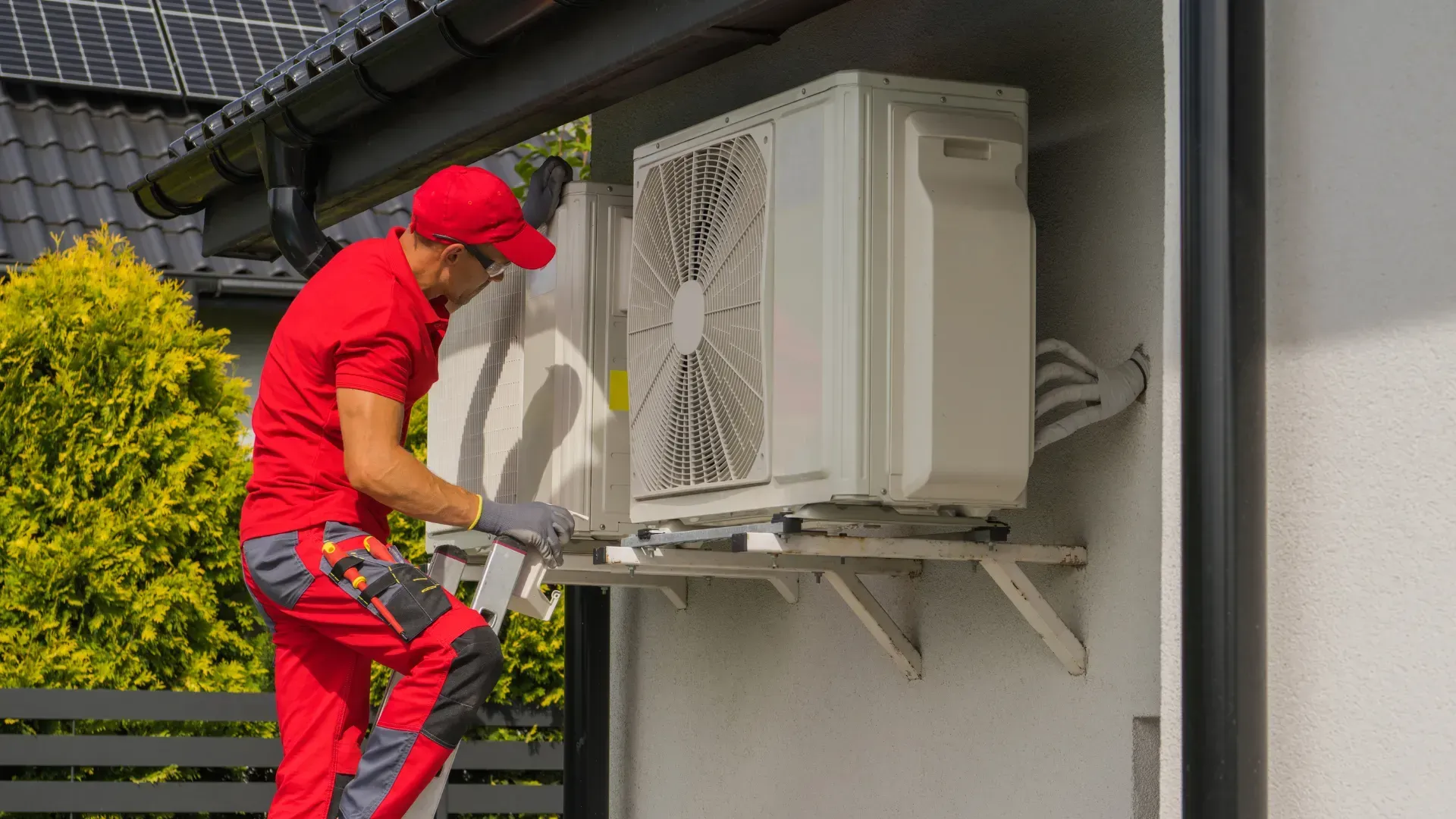 A man is installing an air conditioner on the side of a house.