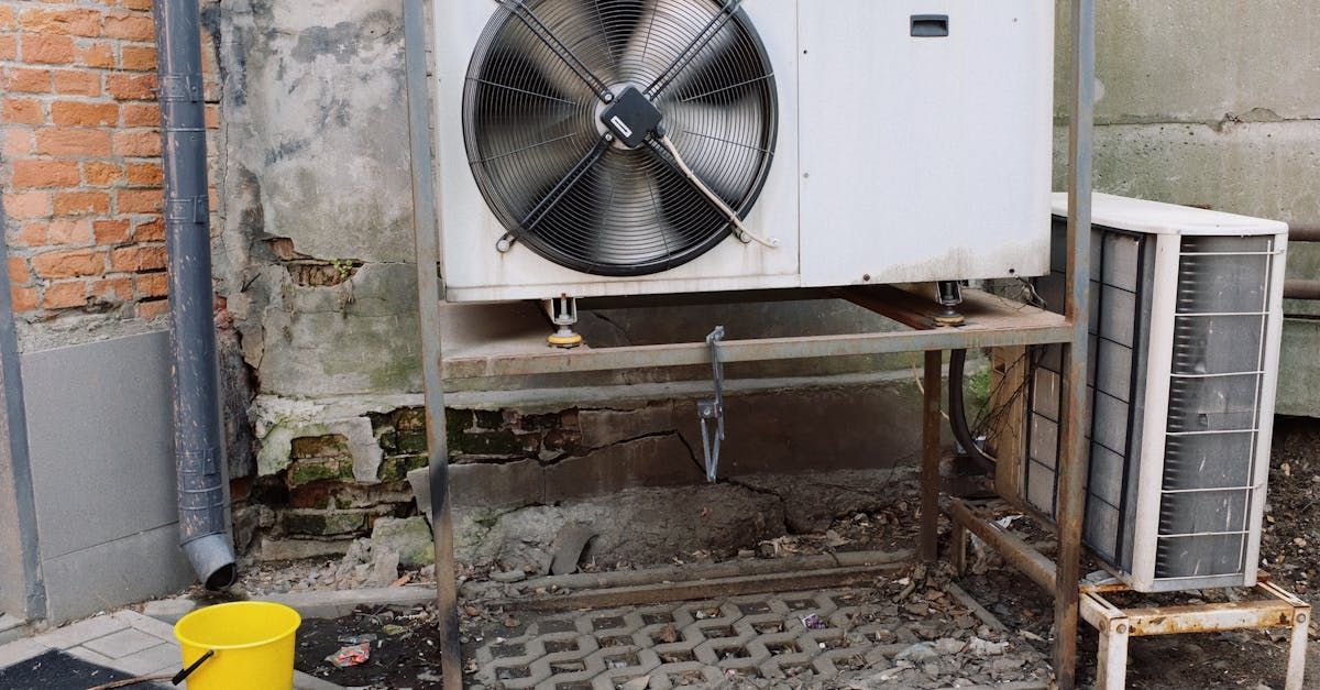 A large fan is sitting on top of a metal stand next to a yellow bucket.