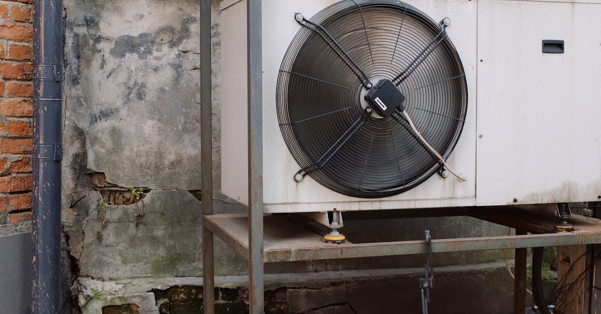 A large fan is sitting next to a brick wall.