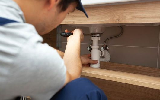 A plumber is fixing a sink in a bathroom.