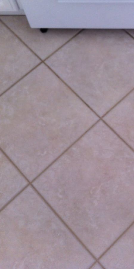 A close up of a tiled floor with a washing machine in the background.