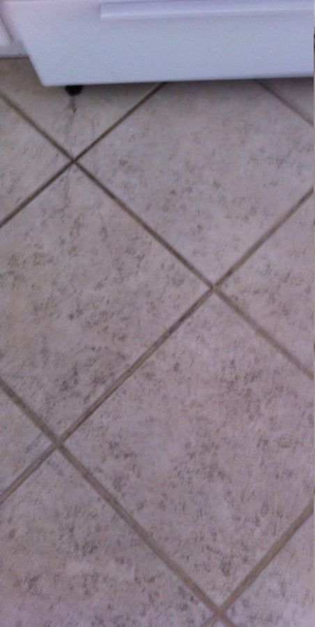 A close up of a tiled floor with a white appliance in the background.