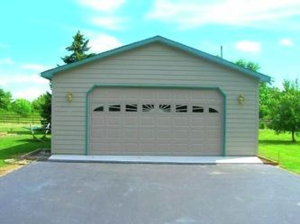 Tan garage with green trim and a paved driveway under a blue sky.