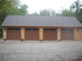 A four-car garage with brown doors and a dark roof on a gravel driveway.