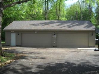 Tan garage with three bays and a door; asphalt driveway, trees in the background.