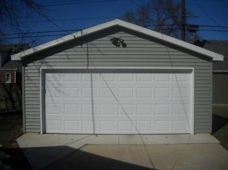 Gray garage with white door and trim, set on concrete, under blue sky.
