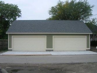 Two-car garage with light green siding, two white garage doors, gray roof, and a concrete driveway.