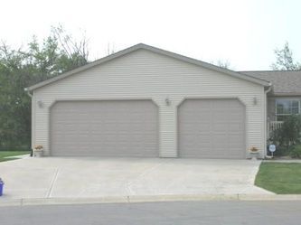 Tan two-car garage with concrete driveway, small bushes, and green grass.