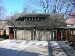 Two-car garage with tan doors, brown roof, and red side doors. Concrete driveway.