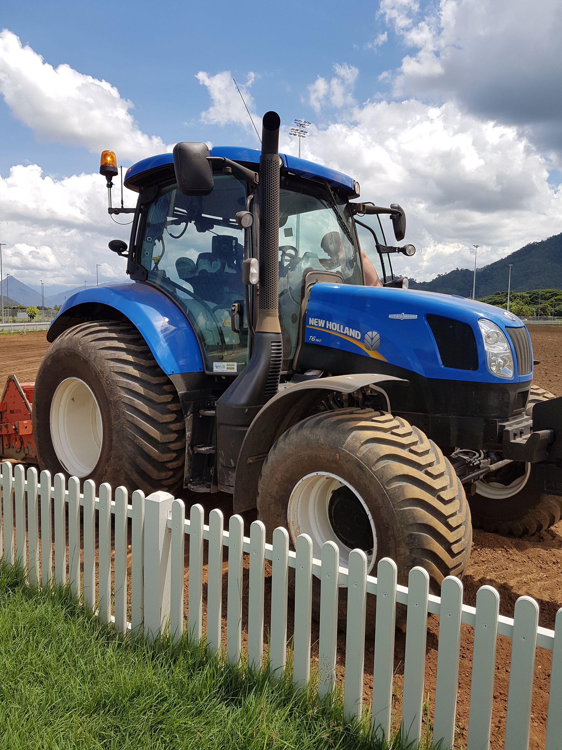 A blue tractor is parked in front of a white picket fence.