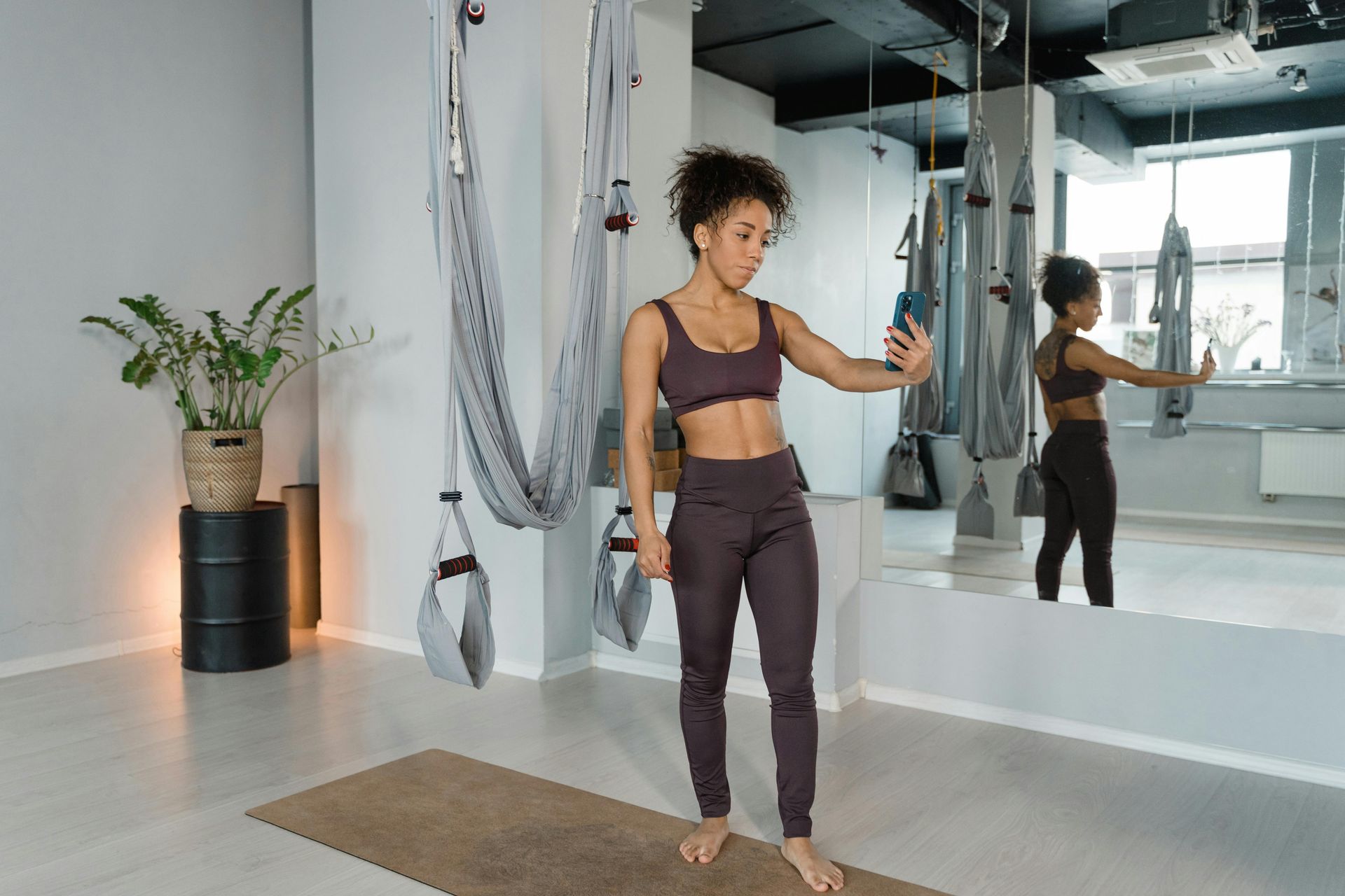 A woman is taking a selfie in a gym while doing aerial yoga.