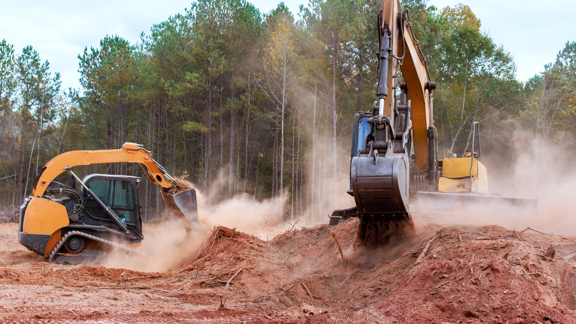 Two yellow excavators digging in red dirt, with trees in the background, creating dust.