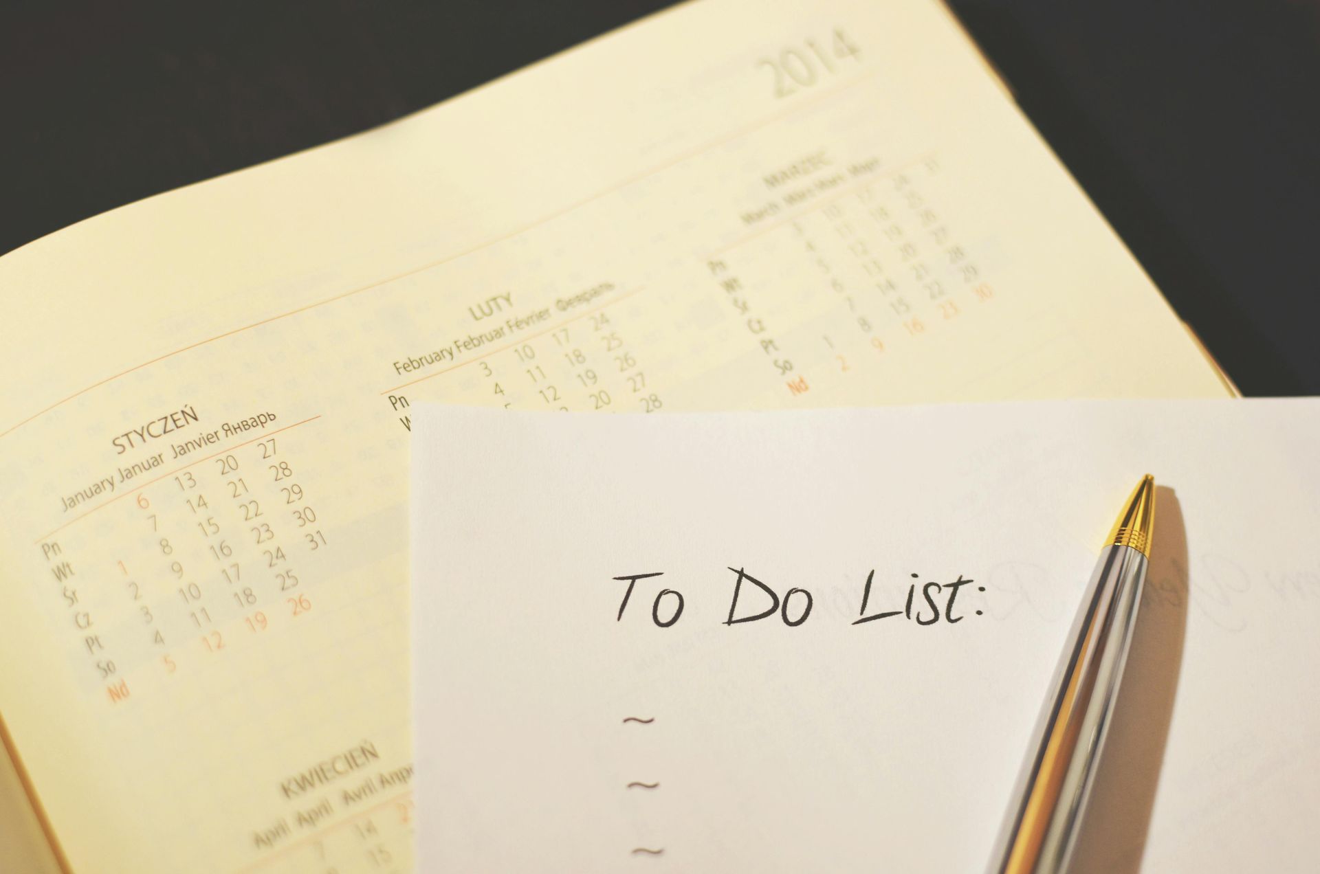 To-do list on paper with a pen, calendar in the background.