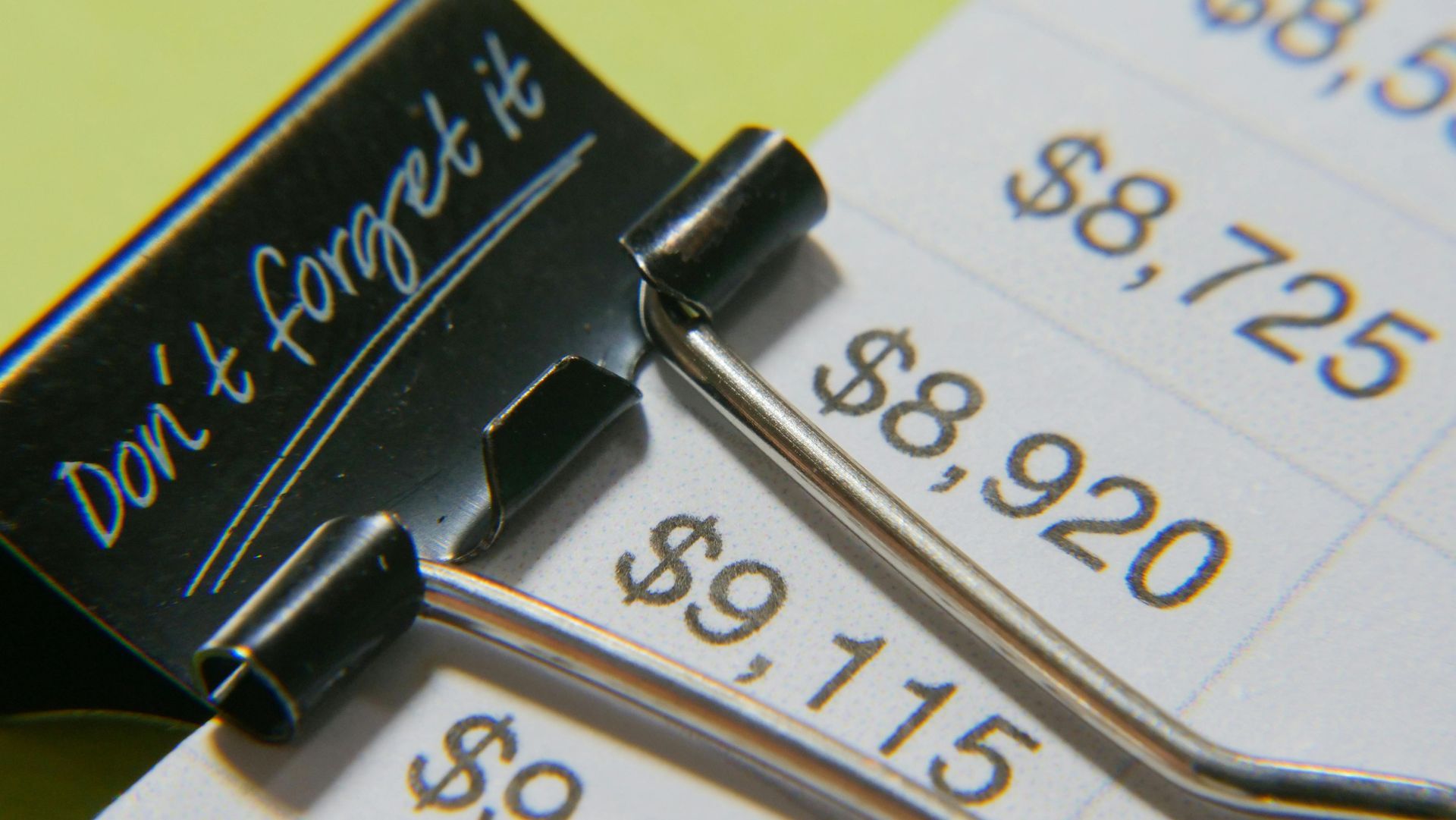 Binder clip holding financial document with dollar amounts, “Don’t Forget It” written on clip.