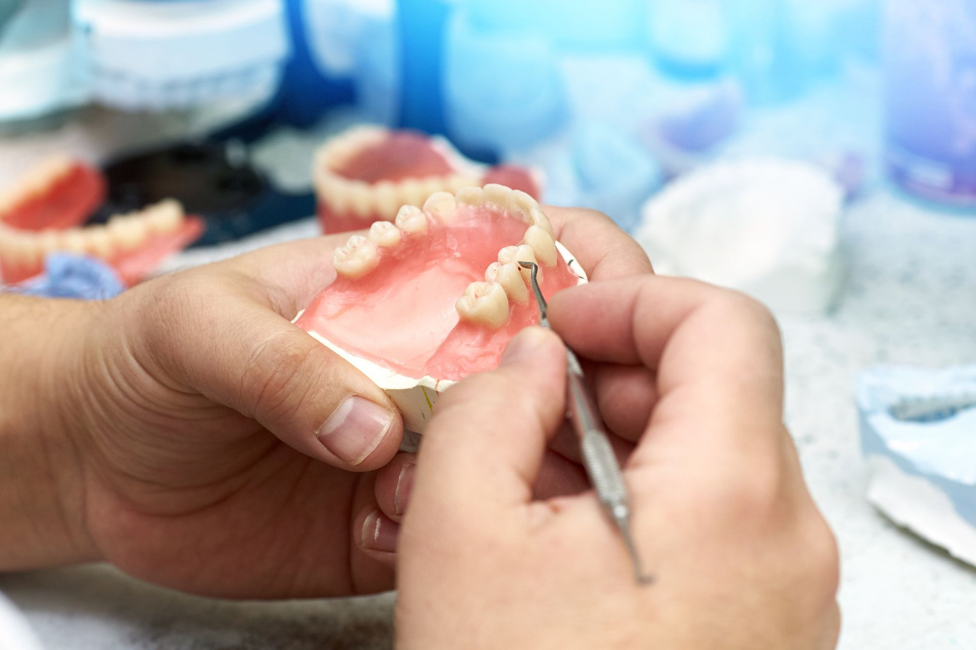 Dentist working on dentures with a small tool, pink and white setting in a lab.