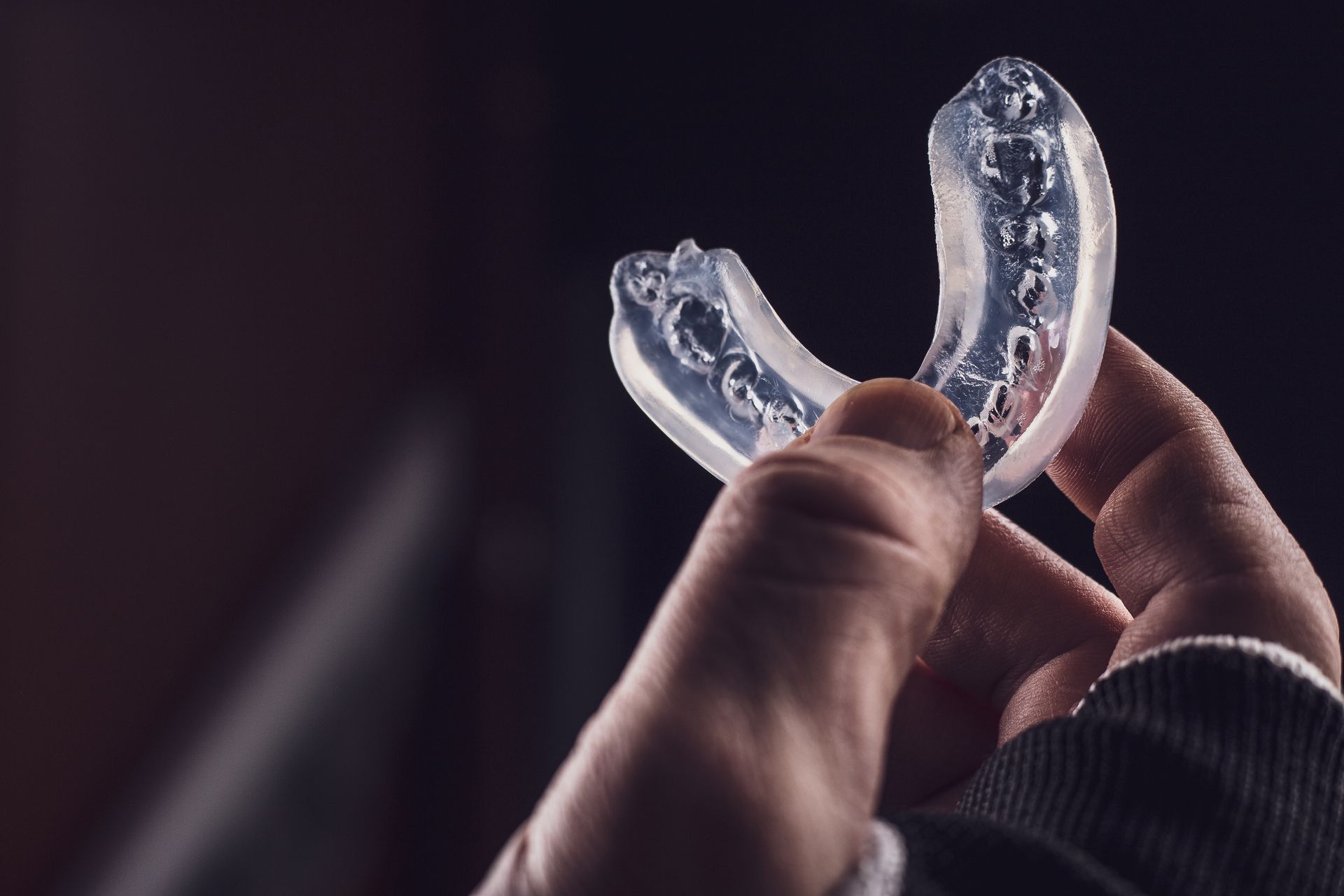 Hand holding a clear, molded mouthguard against a dark background.