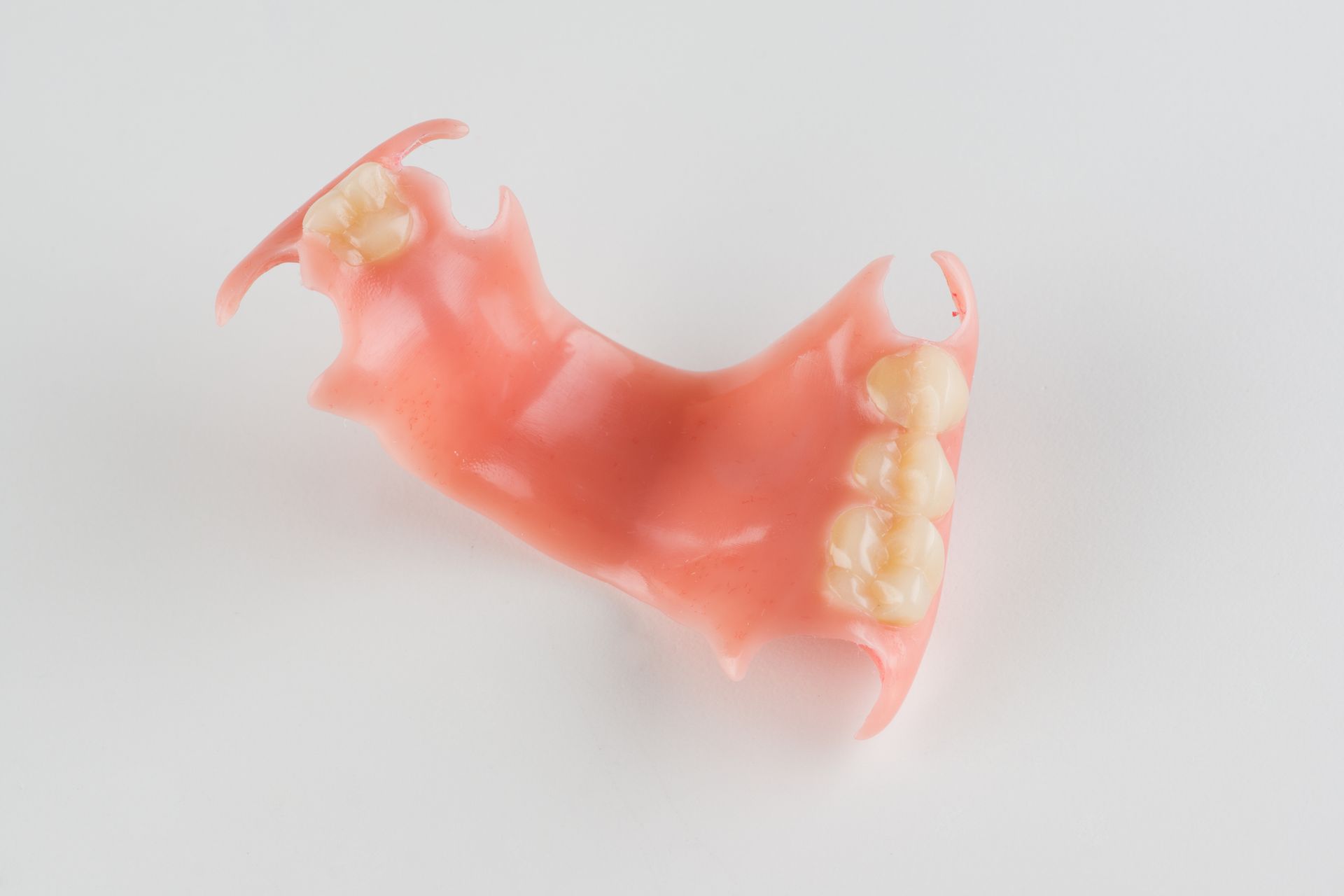Partial denture, pink plastic with three artificial teeth, on a white surface.