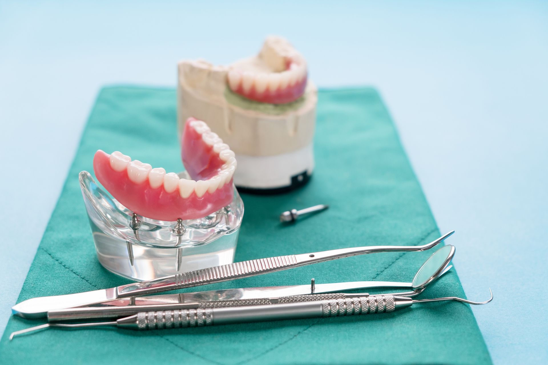 Dentures and dental tools on a green cloth, with a light blue background.