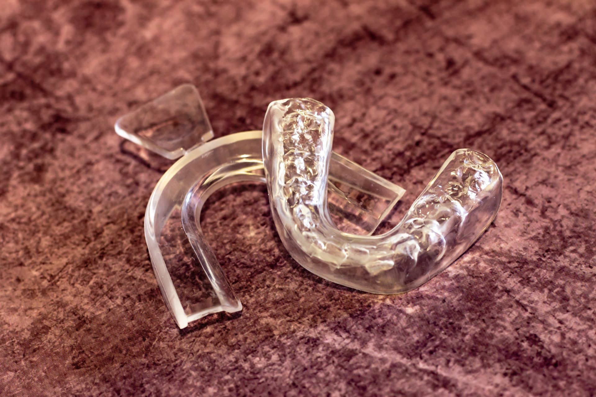 Two clear plastic mouth guards on a maroon surface.