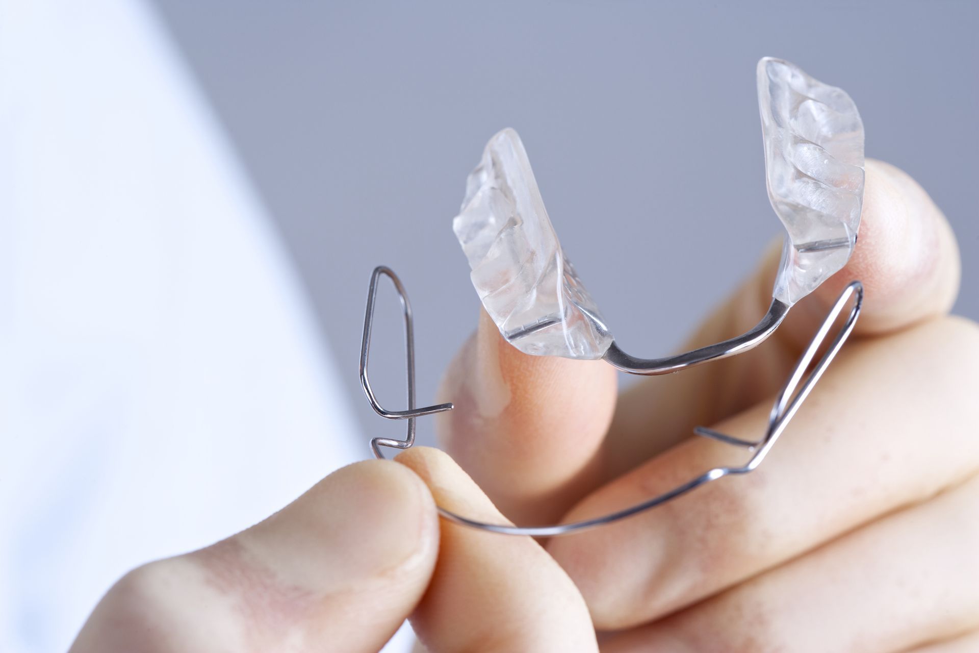 Hand holding a clear dental retainer with metal wires.