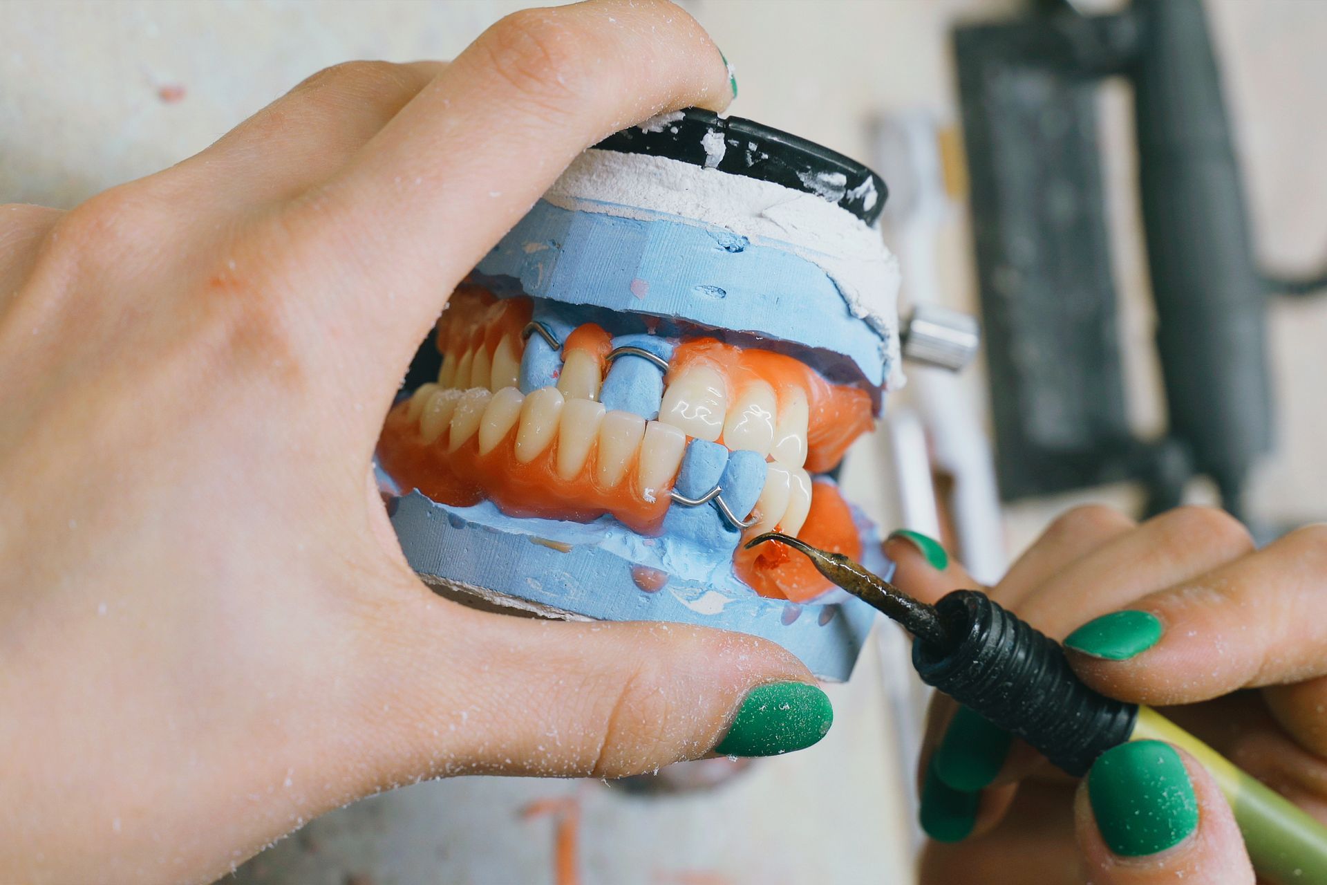 Person carving a wax denture model, with a dental lab setting.