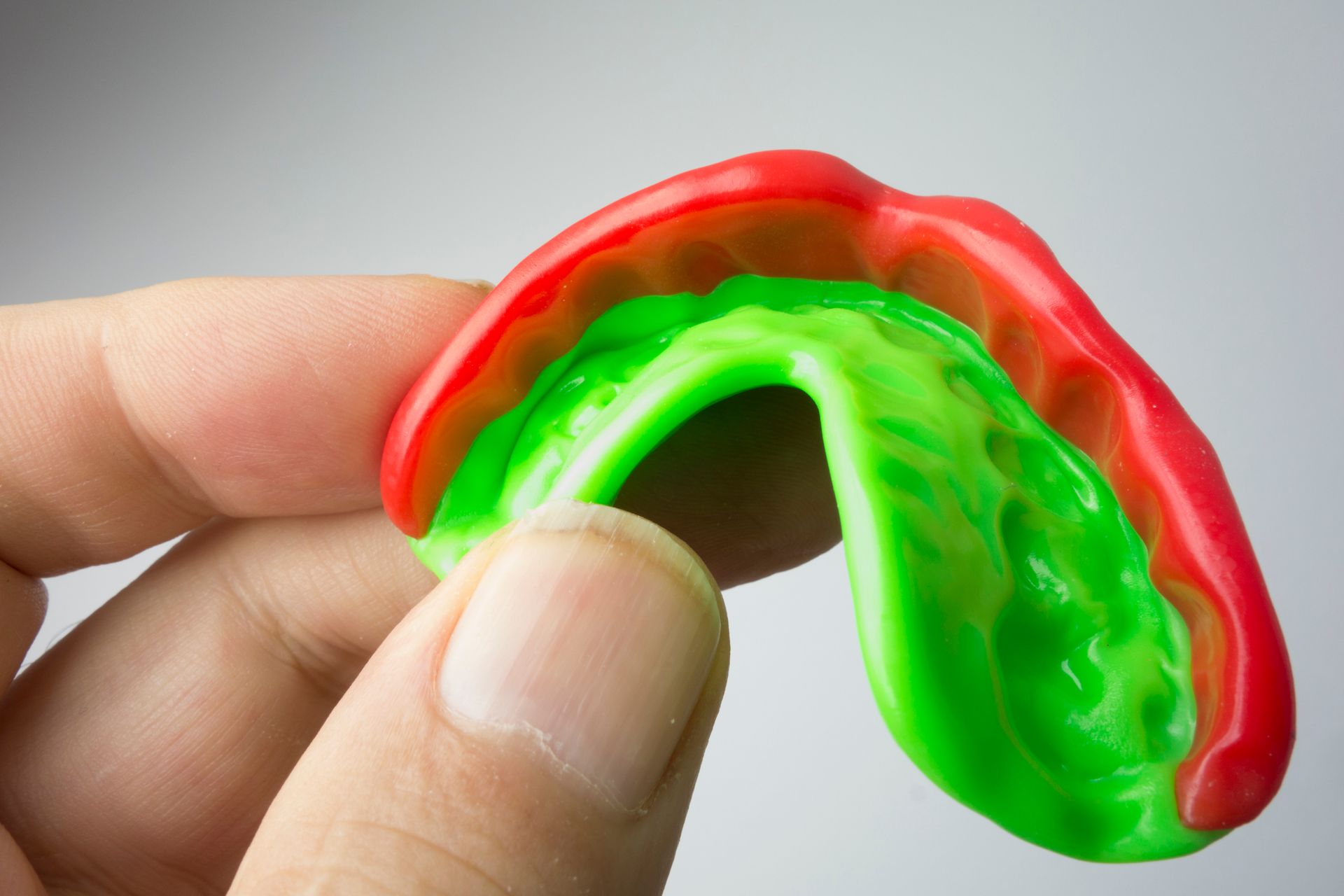 Hand holding a red and green mouthguard, close-up view.