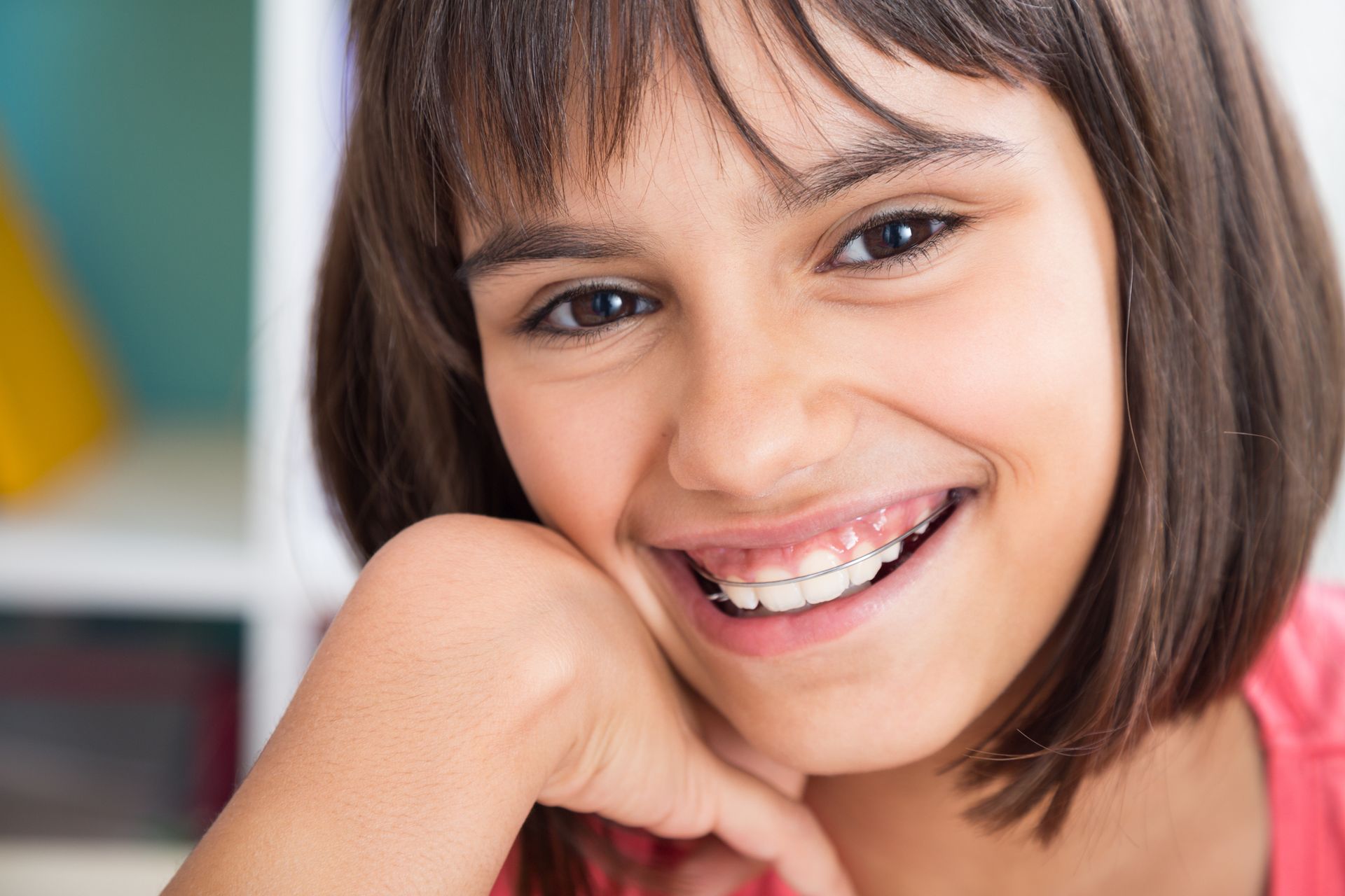 Smiling girl with braces resting chin on hand.