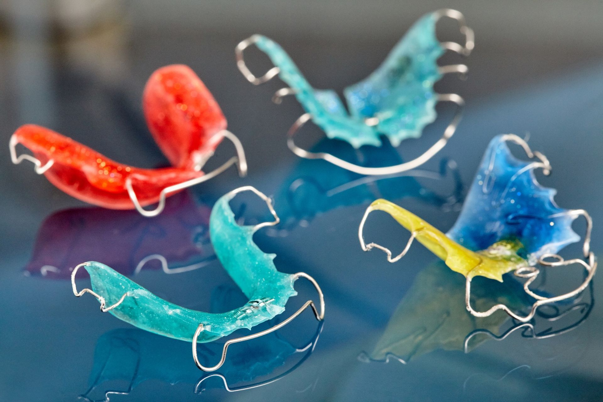 Four colorful orthodontic retainers on a reflective surface.