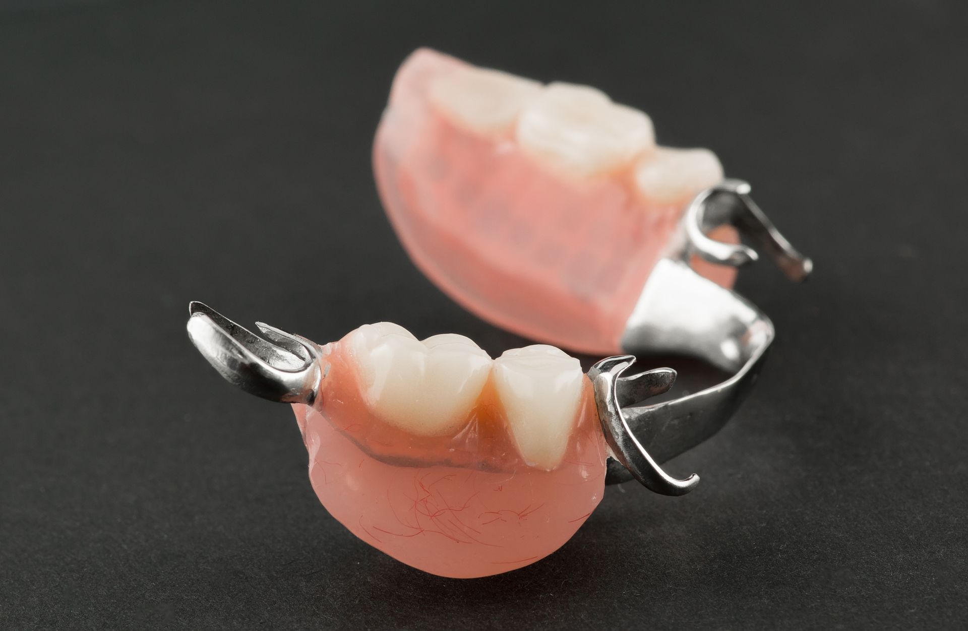 Partial dentures with pink base and metal clasps on a dark surface.