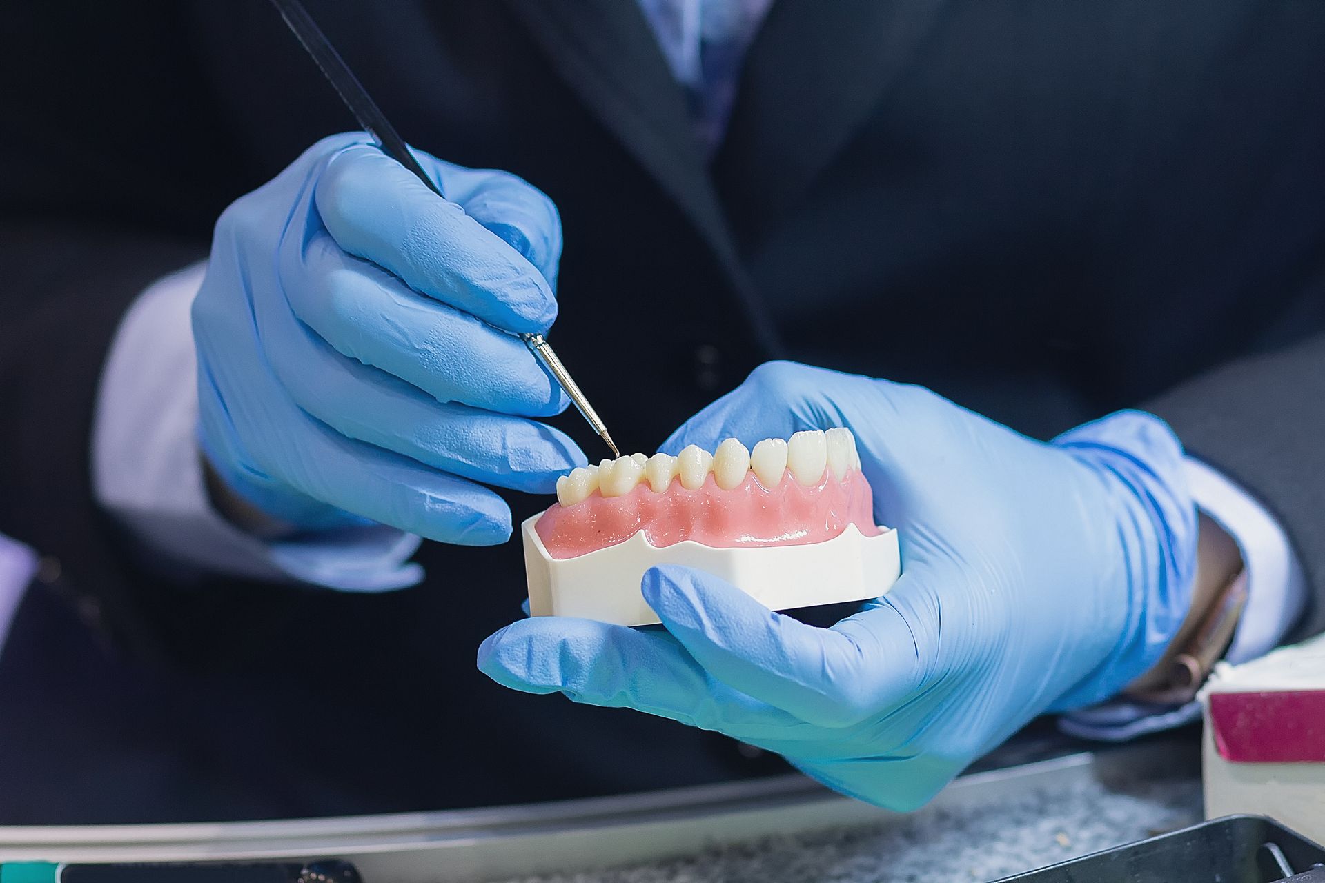 Person in blue gloves working on dentures with a brush.