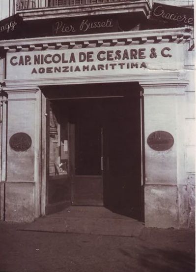 Una donna con le cuffie sorride alla telecamera, seduta a una scrivania. Si trova in un ufficio con una mappa del mondo e un globo sullo sfondo.