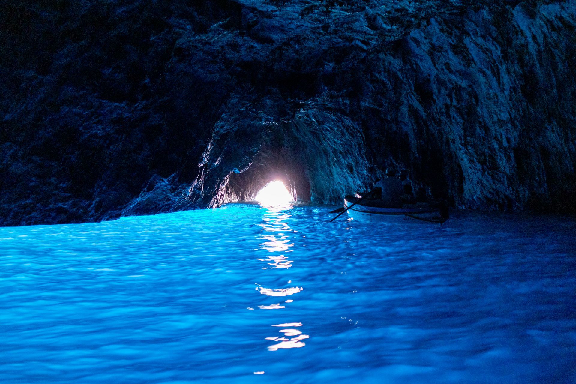 Acqua di un azzurro brillante all'interno di una grotta buia, con la luce che filtra dall'apertura della grotta.